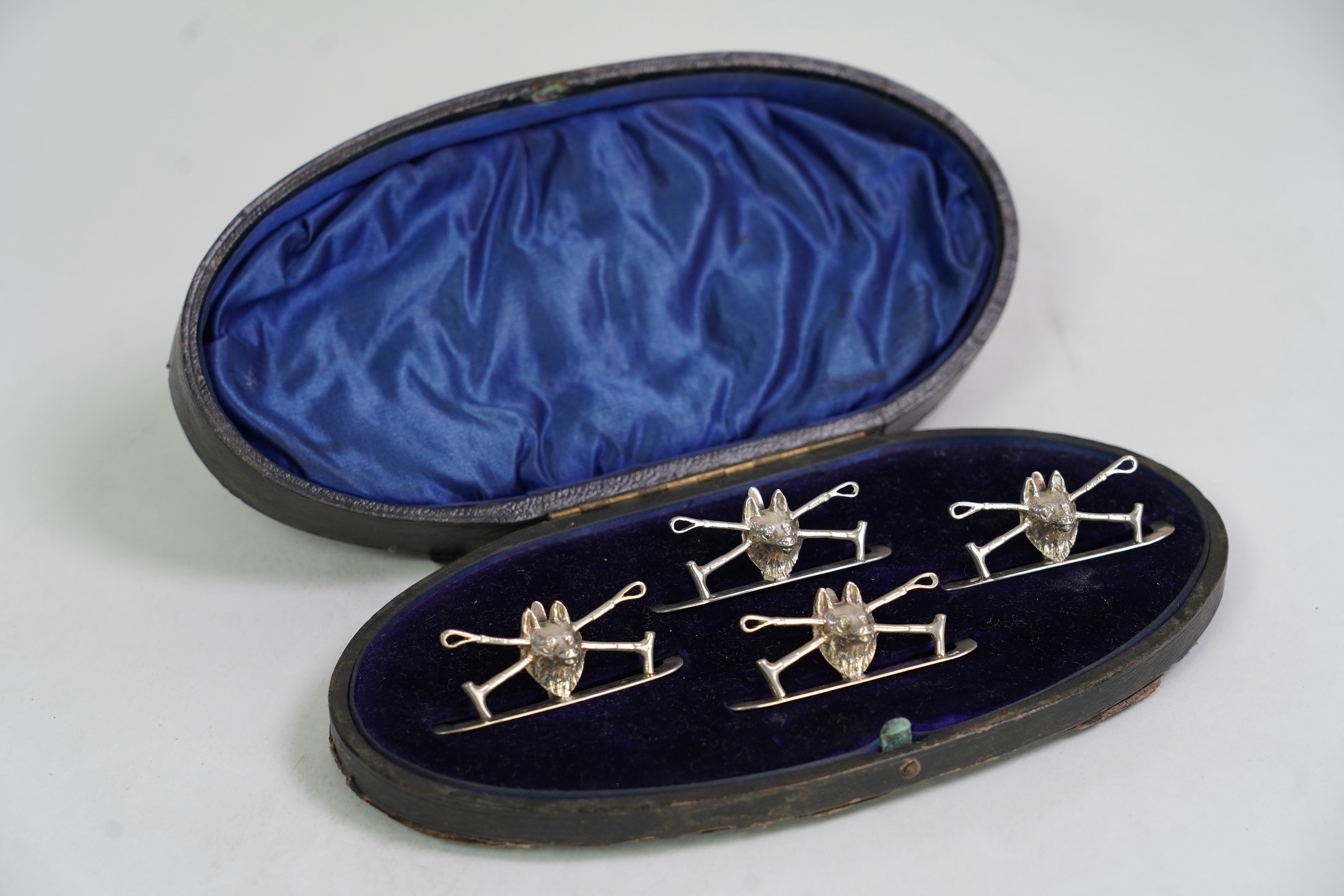 A cased set of four George V silver menu holders, modelled as a fox head with crossed riding crops, by William Hutton & Sons